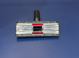 Oreck Ironman vacuum cleaner head on a blue surface, featuring transparent compartments and red detailing for strong suction.