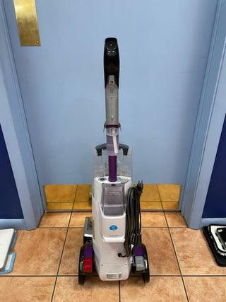 A certified refurbished Hoover Smartwash Pet Complete Carpet Cleaner stands upright in a room with blue walls and tiled flooring.