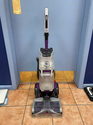 A purple and gray upright Sew & Vac Hoover Smartwash Pet Complete Carpet Cleaner, in great working condition, stands against a blue wall with yellow accents.