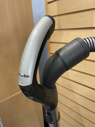 Close-up of a Sew & Vac Certified Refurbished Miele C3 Brilliant electric vehicle charging plug mounted on a stand, with a wooden background.