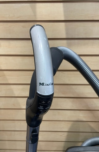Close-up of a certified refurbished Sew & Vac Miele C3 Brilliant vacuum cleaner handle with control settings, set against a wooden panel background.