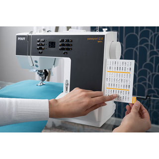 A person chooses a stitch from the reference card on the PFAFF Pfaff Passport 2.0 sewing machine while working with blue fabric.