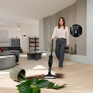 A woman uses the Miele Triflex HX3 Cordless Stick Vacuum in Brilliant White by 2-Miele to clean spilled soil and a fallen plant in a modern living room. An inset shows a close-up of the vacuum’s settings, highlighting its advanced HEPA filter for cleaner air.