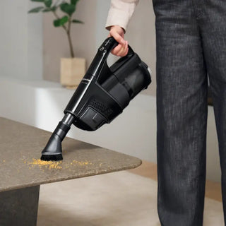 A person uses the 2-Miele Miele Triflex HX3 Cordless Stick Vacuum in Brilliant White, featuring a HEPA filter, to remove crumbs from the edge of a table.