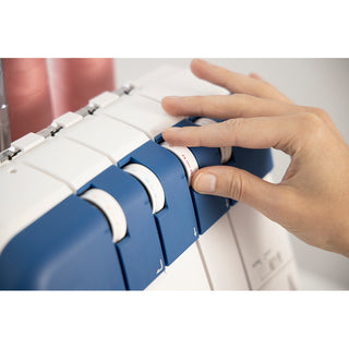 A hand adjusts a blue tension dial on the Husqvarna Viking Amber Air S400 Overlock Machine by Husqvarna Viking, with pink thread spools in the background.