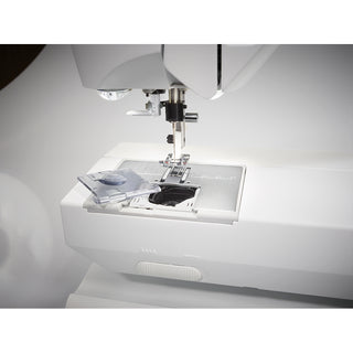 Close-up of a Husqvarna Viking Opal 650 sewing machine by Husqvarna Viking, showing its open bobbin case cover with the bobbin compartment and surrounding metal plate visible.