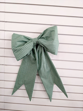A large green bow with white polka dots and long tails, perfect for beginners, is displayed against a white slatted wall—showcase your skills from the 1000-Education Big Bow Class at LAYTON LOCATION on Feb 21, 2026 (2–4 pm) with instructor Kathi.