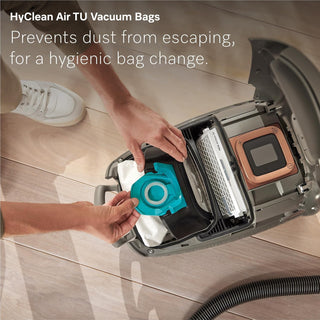 A person inserts a blue vacuum bag into an open 2-Miele Miele Guard L1 Electro canister vacuum on a wooden floor, highlighting hygienic dust containment and the superior AirClean Filter for deep carpet cleaning.