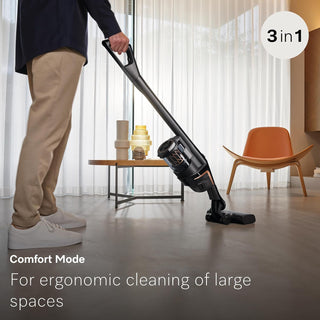 A person uses the 2-Miele Triflex HX2 Pro 3-in-1 Cordless Stick Vacuum with a HEPA Lifetime Filter on a light-colored floor in a modern, minimally furnished living room filled with bright natural light.