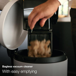 A person empties debris and pet hair from a 2-Miele Boost CX1 Cat & Dog bagless vacuum cleaner into a bin. Text reads: “Bagless vacuum cleaner with simple emptying and powerful pet hair removal.”.