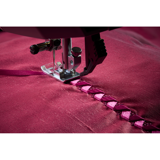 Close-up of the 38-SVP - Singer Viking Pfaff Creative Expression 750 sewing machine customizing stitches to attach pink ribbon onto pink fabric, forming a decorative braided pattern.