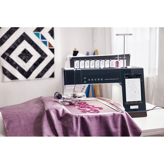 The Pfaff Creative Performance 950 from Imagine Sewing & Vacuum stitches a pink floral pattern onto purple fabric, with design options shown on its touchscreen in a well-lit sewing room.