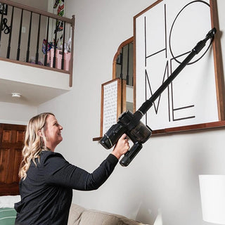 Using her Riccar R65 Cordless Stick Vacuum with SupraCyclonic™ filtration, a woman effortlessly cleans a framed wall art piece at home.