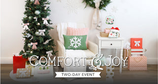 A festive room with a decorated tree, wrapped gifts, and a cozy chair sets the scene for Sew & Vac's Kimberbell Comfort & Joy-2 Day Event. "COMFORT & JOY, TWO-DAY EVENT" text is displayed over the image.