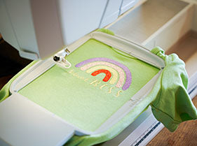 A green shirt with a rainbow on it, embroidered using a Bag of Tricks machine.