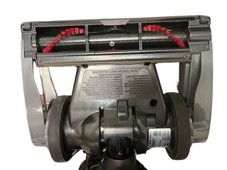 The underside of a refurbished Oreck Discover vacuum cleaner from Imagine Sewing & Vacuum displays the brush roll, two wheels, and safety instruction label. This lightweight vacuum is engineered for easy maneuverability and dependable cleaning performance.