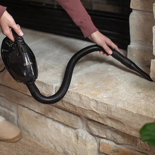A woman using attachments to vacuum clean a fireplace with the Riccar GEM Handheld Vacuum by Riccar.