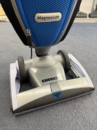 Close-up of a Sew & Vac Oreck Magnesium LW1500RS (Certified Refurbished) vacuum cleaner with a new HEPA bag on carpet, highlighting the brand name and part of the vacuum head.