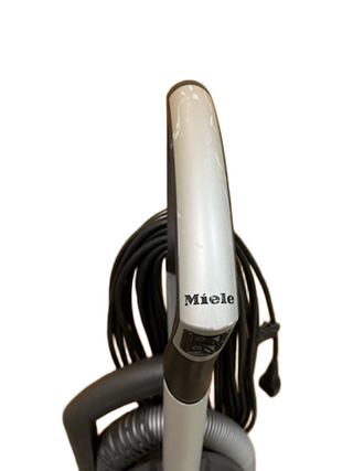 Close-up of the Miele Dynamic U1 Fresh Air PowerLine upright vacuum handle by Imagine Sewing & Vacuum, showing attached hose, power cord wrapped around the back, and AirClean filters for superior filtration.