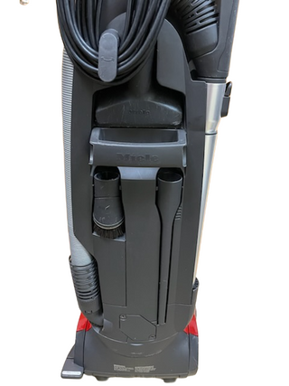 The Miele Dynamic U1 Fresh Air PowerLine upright vacuum from Imagine Sewing & Vacuum stands upright with an attached hose, top-wrapped power cord, AirClean filters, and accessory tools stored on the back.