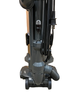 A close-up view of the lower section of the Shark Professional Navigator Lift-Away UV550 Upright Vacuum by Imagine Sewing & Vacuum, highlighting its gray body, cord, wheels, and hose attachment.