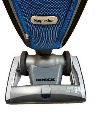 A close-up of the base of an Oreck Magnesium vacuum by Imagine Sewing & Vacuum, showing its blue and silver body with clear "Magnesium" and "ORECK" labels, plus a new bag for optimal performance.