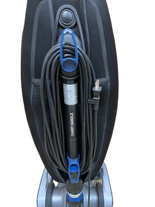 A close-up of the Oreck Magnesium by Imagine Sewing & Vacuum shows its power cord neatly wrapped around the carry handle, highlighting a refurbished unit with a new brushroll in good condition.