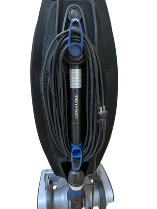 Refurbished Oreck Magnesium upright vacuum cleaner from Imagine Sewing & Vacuum, featuring a power cord neatly wrapped around hooks and a handle labeled "CARRY HANDLE.