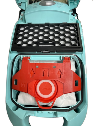 The refurbished Miele Neptune by Imagine Sewing & Vacuum features an open red dust bag holder, a white dust bag inside, and a black honeycomb filter on top.