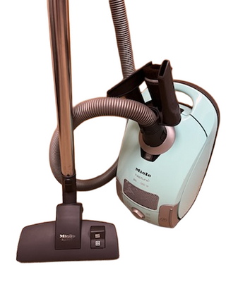 A reconditioned Miele Neptune canister vacuum from Imagine Sewing & Vacuum in light blue, featuring a hose, metal wand, and black floor brush attachment.