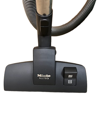 Close-up of an Imagine Sewing & Vacuum Miele Neptune refurbished vacuum floor head with a hose attached and a button on the right side.
