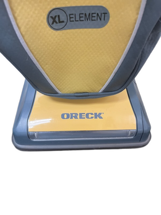Close-up of the Oreck XL Element vacuum, featuring the base with its logo and a yellow-gray bag. Sold by Imagine Sewing & Vacuum, it's a top pick for those seeking reliability on hard floors.
