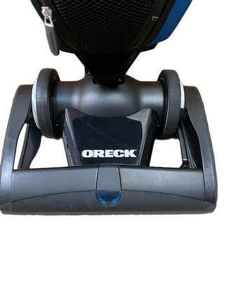 A close-up of the front bottom of a refurbished Oreck Magnesium LW100 vacuum cleaner from Imagine Sewing & Vacuum, highlighting the wheels and Oreck logo.