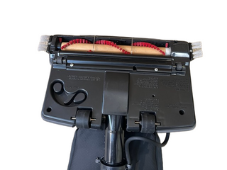 Bottom view of the Oreck XL Platinum vacuum head by Imagine Sewing & Vacuum, showing its roller brush, two wheels, belt, and a pair of scissors attached inside the casing.