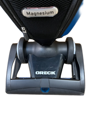 Close-up of the Oreck Magnesium LW100 vacuum base by Imagine Sewing & Vacuum, showing "Magnesium" and "ORECK" labels and spotlighting its never ending belt design.