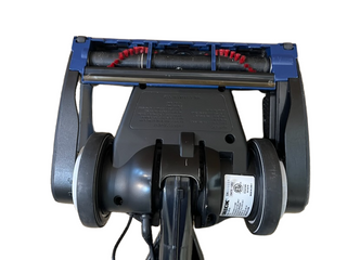 Bottom view of the refurbished Oreck Magnesium LW100 vacuum cleaner head by Imagine Sewing & Vacuum, showing two large wheels, a never ending belt, red-bristled rotating brush, and a certification label.