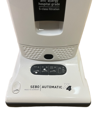 White upright Sebo X4 vacuum base with a control panel showing status indicators for brush height and maintenance alerts.