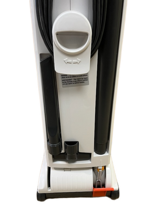 Back view of a refurbished Sebo X4 vacuum showing an integrated cord wrap, an accessory crevice tool, and an orange foot pedal.