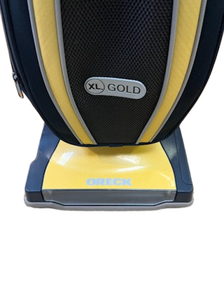 Close-up of a lightweight, two-speed yellow and black Oreck XL Gold upright vacuum, showing the “XL GOLD” label on the bag housing and the brand name on the base.