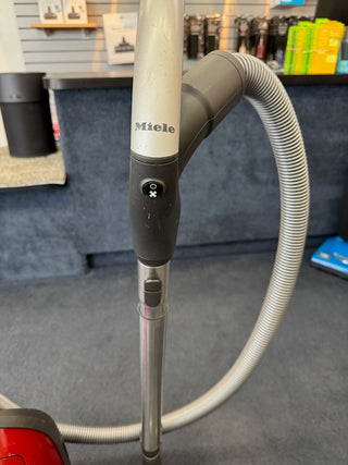 A close-up of a Sew & Vac Used Miele Complete C3 Canister Vacuum handle and hose with a power button, featuring HEPA filtration, displayed in a store setting.
