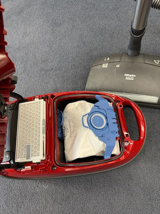 Open red Sew & Vac Used Miele Complete C3 Canister Vacuum displays a fitted dust bag and HEPA filter inside, with the premium power head labeled "Miele" resting on carpet nearby.