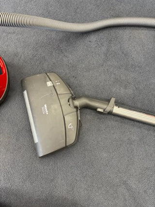 A Sew & Vac Used Miele Complete C3 Canister Vacuum is shown on a carpeted floor, featuring the red body, gray hose, and premium power head.