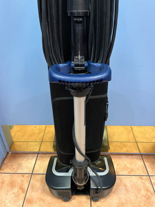 A Certified Refurbished Sew & Vac Oreck Elevate Conquer upright vacuum cleaner on a tiled floor, viewed from the front with its cord retracted.