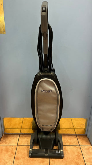 An upright, reconditioned Sew & Vac Oreck Discover UK30500PC vacuum cleaner positioned in a room with yellow walls and tiled flooring.