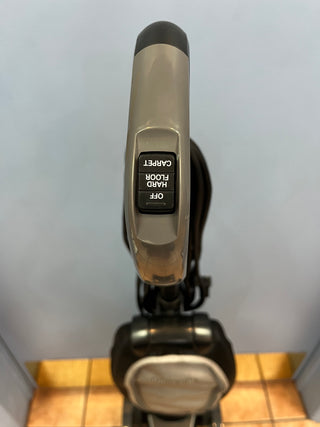 Close-up view of a Sew & Vac Oreck Discover UK30500PC vacuum cleaner handle and part of the tube, facing downward, with the brand name visible and a tile floor in the background.