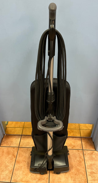 Sew & Vac's Oreck XL21 upright vacuum cleaner with attached hose and HEPA CC bag, parked on a tiled floor against a plain wall.