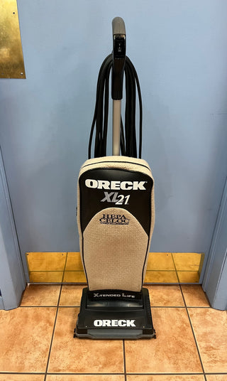 A certified refurbished Sew & Vac XL21 upright vacuum cleaner, beige and black, on a blue tile floor against a light blue wall.