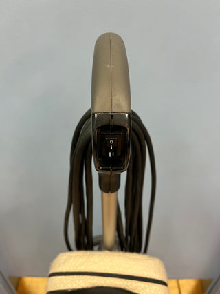 Close-up of a Sew & Vac Certified Refurbished Oreck XL21 silver and black electric shaver head showing the power button, surrounded by two metallic loops against a light background.