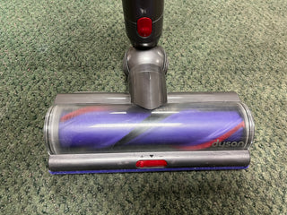 A certified refurbished Sew & Vac Dyson Cyclone v10 Animal vacuum cleaner head on a green carpet, viewed from above, showing details of its roller and casing.