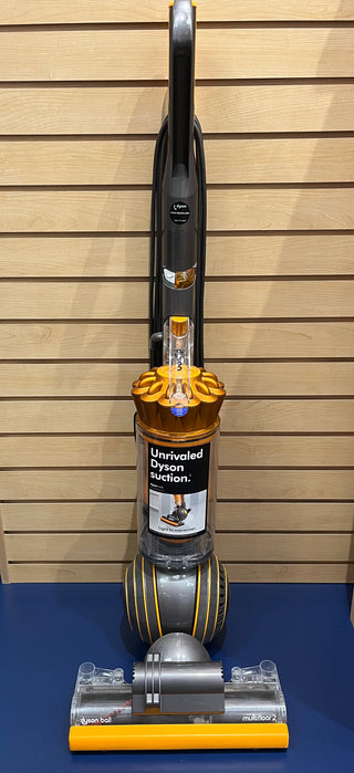 An upright Sew & Vac Dyson UP19 Multifloor 2 vacuum cleaner, almost like new, is displayed against a wood panel wall. The vacuum features a yellow and silver design with "Unrivaled Dyson suction" text on the front and comes with brand new filters.